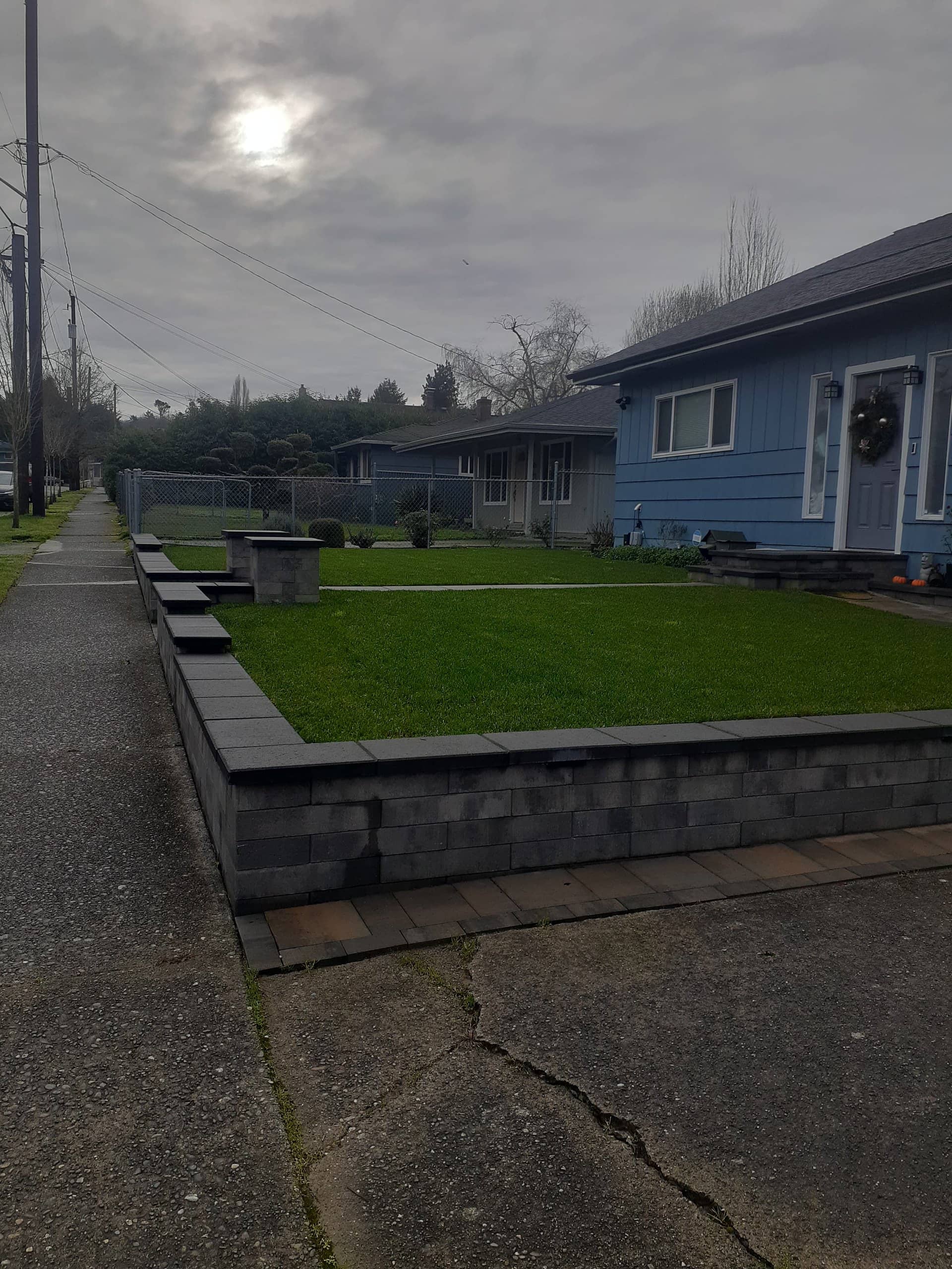 Front-yard block retaining wall with fresh lawn, overcast dusk